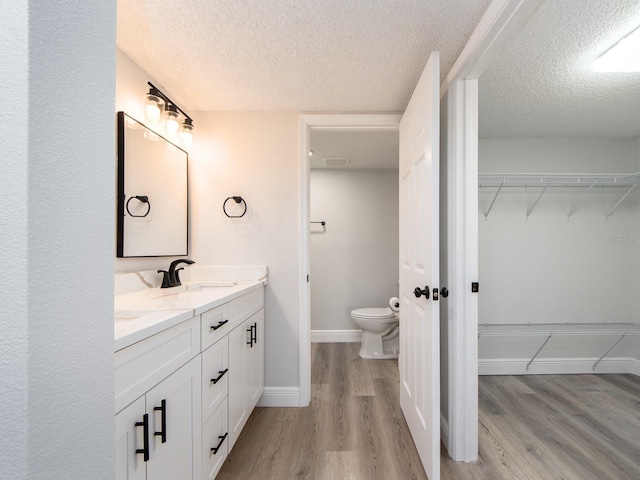 bathroom featuring a sink, toilet, wood finished floors, and a spacious closet