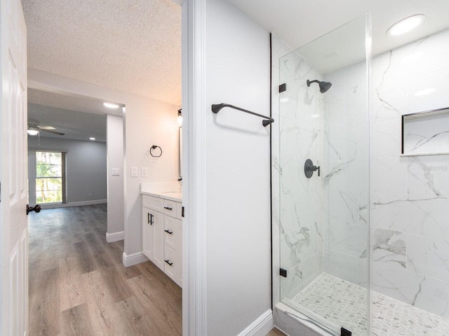 full bath with vanity, wood finished floors, baseboards, a marble finish shower, and a textured ceiling