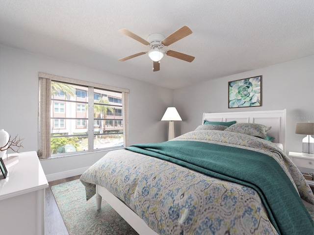 bedroom featuring a ceiling fan, wood finished floors, baseboards, and a textured ceiling