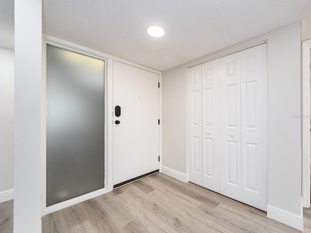 entryway with baseboards, a textured ceiling, and light wood-style floors