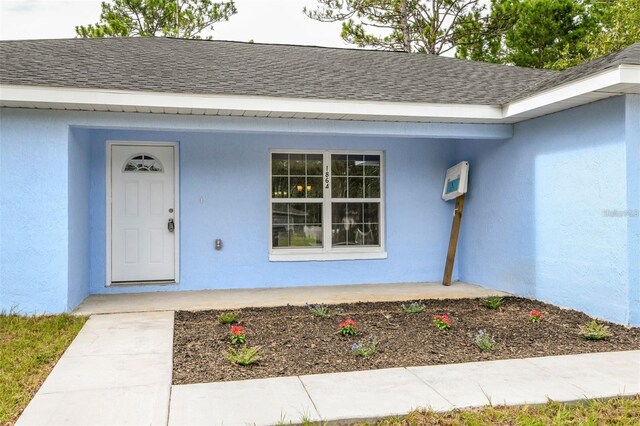 doorway to property featuring stucco siding and a shingled roof