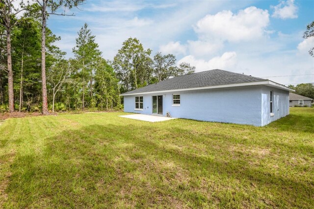 back of property with a shingled roof, a patio area, a lawn, and stucco siding