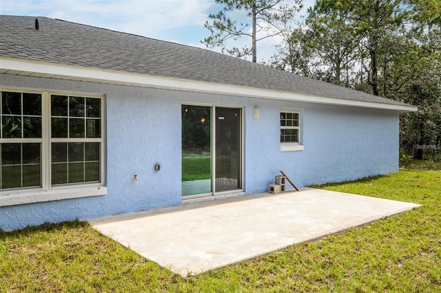 back of property with a yard, stucco siding, a shingled roof, and a patio