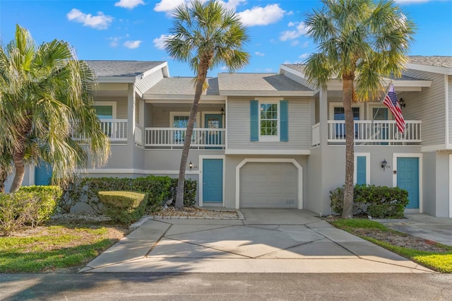 townhome / multi-family property with roof with shingles, a garage, driveway, and stucco siding