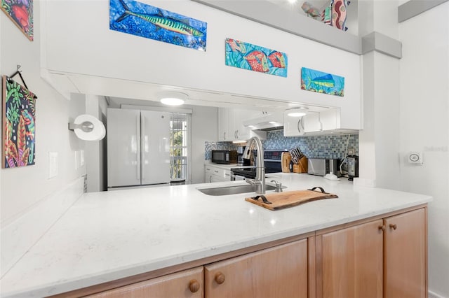 kitchen featuring black microwave, under cabinet range hood, decorative backsplash, freestanding refrigerator, and a sink