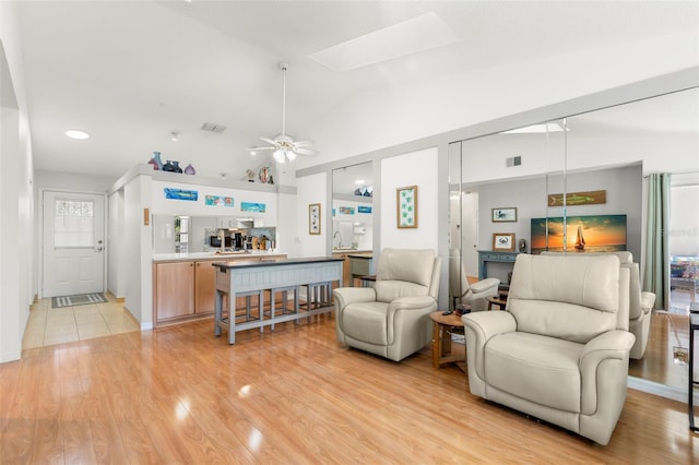 living room featuring lofted ceiling with skylight, light wood-style flooring, a ceiling fan, and visible vents