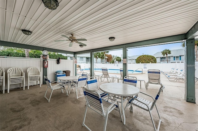 view of patio with outdoor dining space, a community pool, fence, and ceiling fan