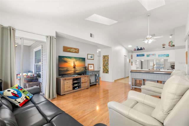 living room with light wood-type flooring, visible vents, vaulted ceiling with skylight, and a ceiling fan