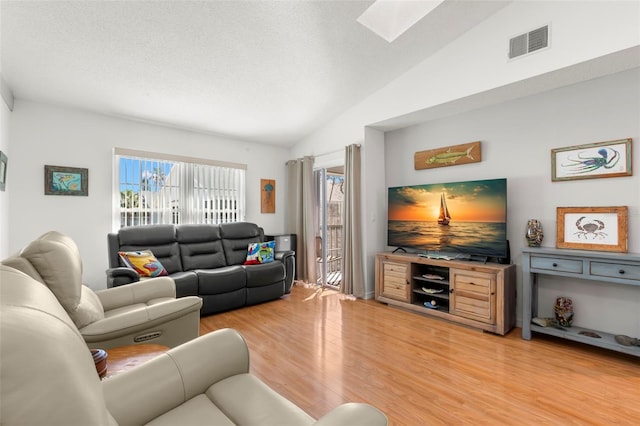 living area featuring lofted ceiling with skylight, visible vents, a textured ceiling, and light wood-type flooring