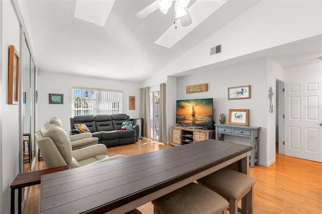 dining space featuring visible vents, lofted ceiling with skylight, light wood-style floors, and a ceiling fan