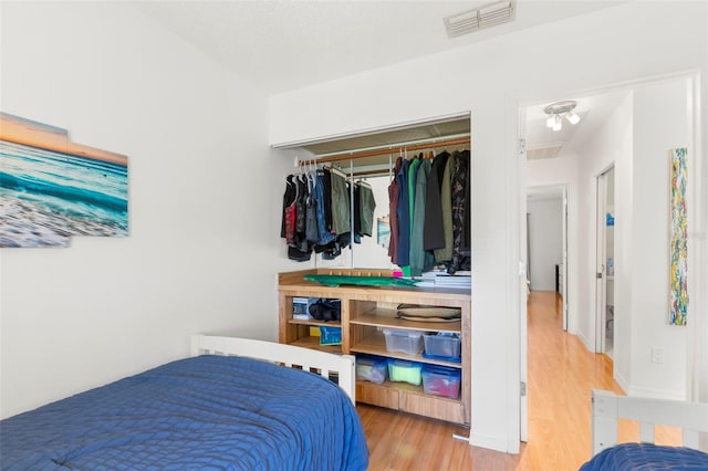 bedroom with wood finished floors, visible vents, and a closet