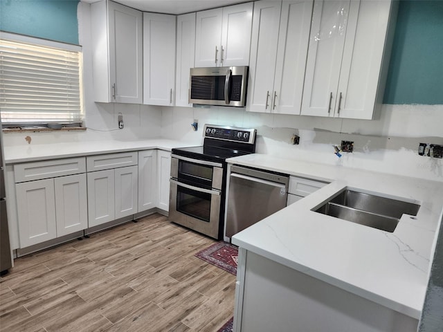 2451 Baywood Dr W, Dunedin, FL 34698 - kitchen with light wood-type flooring, a sink, white cabinetry, appliances with stainless steel finishes, and light stone countertops