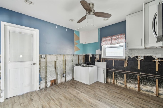 2451 Baywood Dr W, Dunedin, FL 34698 - kitchen featuring light wood-type flooring, a ceiling fan, stainless steel microwave, backsplash, and white cabinets