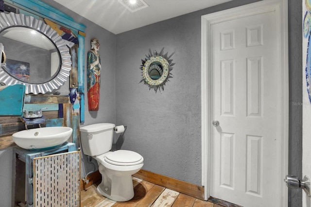 half bath featuring visible vents, baseboards, toilet, a textured wall, and a sink