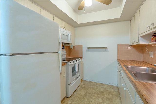 kitchen featuring a ceiling fan, a sink, a tray ceiling, tasteful backsplash, and white appliances