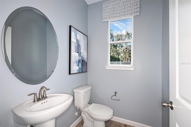 half bath with toilet, wood finished floors, baseboards, and a sink