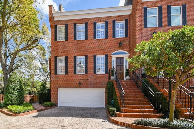 view of front of house with stairs, decorative driveway, brick siding, and an attached garage