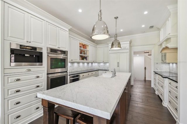 kitchen featuring visible vents, a center island with sink, a sink, double oven, and crown molding