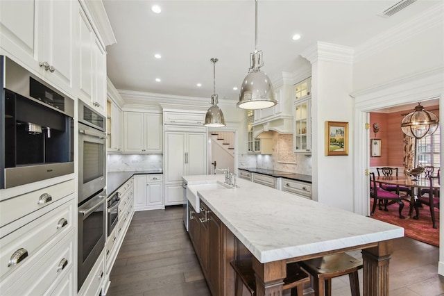 kitchen with visible vents, backsplash, glass insert cabinets, crown molding, and a large island with sink