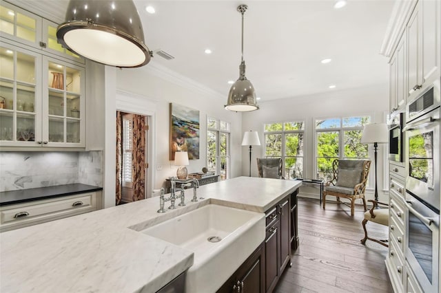 kitchen with a sink, light stone counters, backsplash, dark wood finished floors, and crown molding