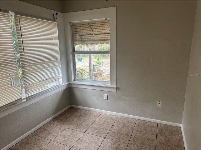 empty room featuring light tile patterned floors, a textured wall, and baseboards