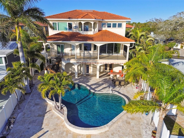 rear view of house with a tile roof, stucco siding, a balcony, an outdoor pool, and a patio