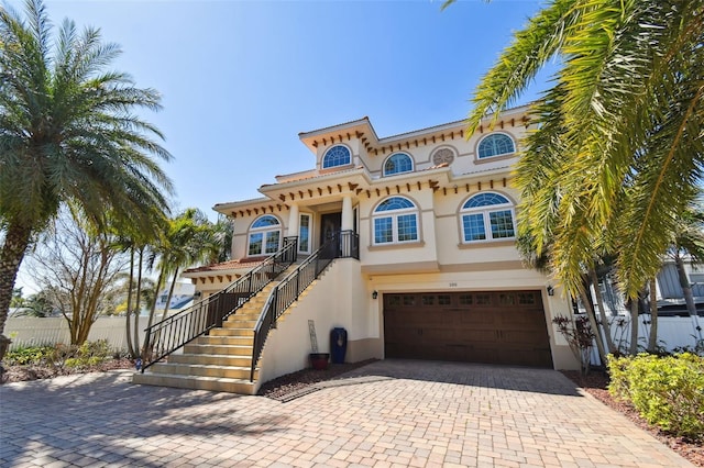 view of front of house with decorative driveway, an attached garage, fence, and stairs