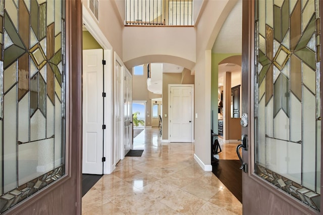 foyer with a high ceiling, arched walkways, baseboards, and marble finish floor