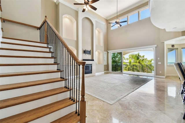 entrance foyer with stairs, a healthy amount of sunlight, a glass covered fireplace, and a ceiling fan