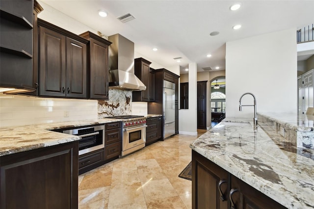 kitchen featuring visible vents, high end appliances, wall chimney exhaust hood, a ceiling fan, and a sink