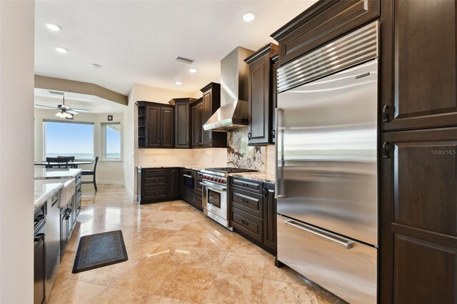 kitchen with visible vents, high quality appliances, dark brown cabinetry, wall chimney exhaust hood, and tasteful backsplash