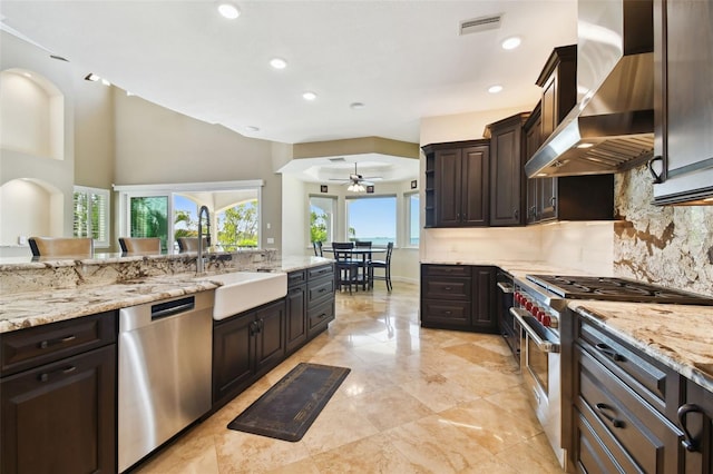 kitchen with backsplash, ceiling fan, dark brown cabinetry, appliances with stainless steel finishes, and wall chimney exhaust hood