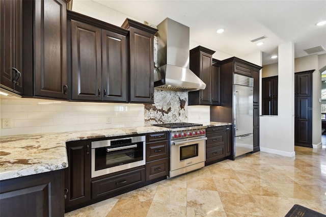 kitchen with visible vents, high quality appliances, light stone counters, wall chimney range hood, and decorative backsplash