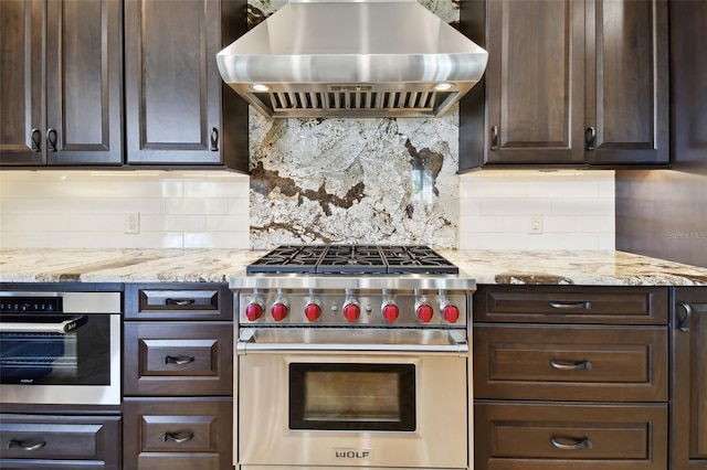 kitchen with dark brown cabinets, appliances with stainless steel finishes, a warming drawer, exhaust hood, and backsplash