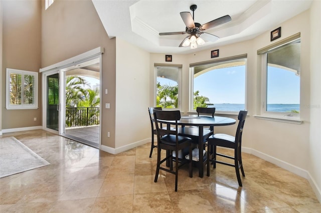 dining area featuring a raised ceiling, baseboards, a water view, and ceiling fan
