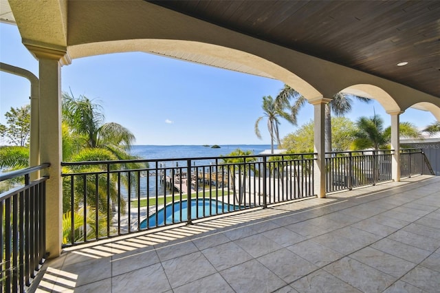 view of patio with a fenced in pool, a balcony, and a water view
