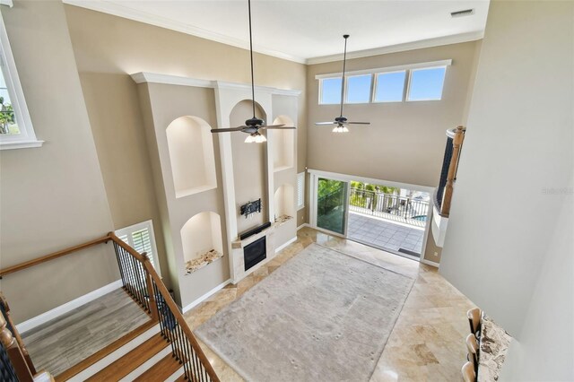living room featuring baseboards, visible vents, a fireplace, ornamental molding, and ceiling fan