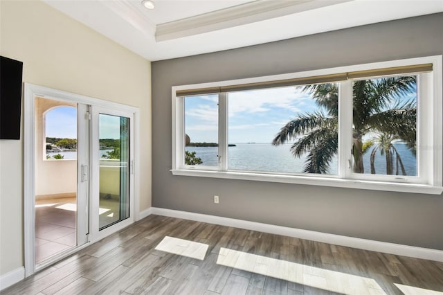 unfurnished room with a water view, a raised ceiling, wood finished floors, crown molding, and baseboards