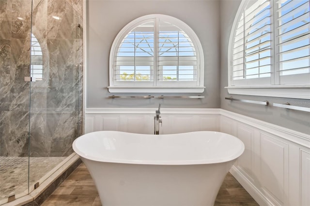 bathroom featuring a marble finish shower, a wainscoted wall, a soaking tub, and wood finished floors