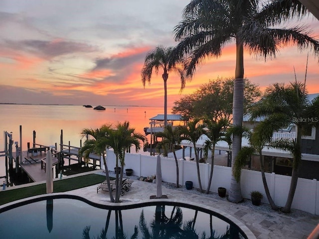 pool at dusk featuring fence, a water view, a patio area, boat lift, and a boat dock