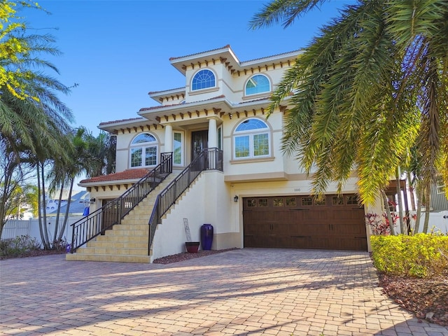 view of front of house with stairway, a tile roof, stucco siding, decorative driveway, and a garage