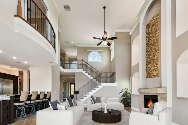 living area with visible vents, stairway, a fireplace, crown molding, and ceiling fan