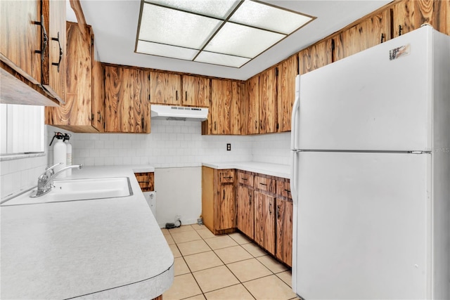 kitchen featuring under cabinet range hood, brown cabinetry, freestanding refrigerator, and a sink