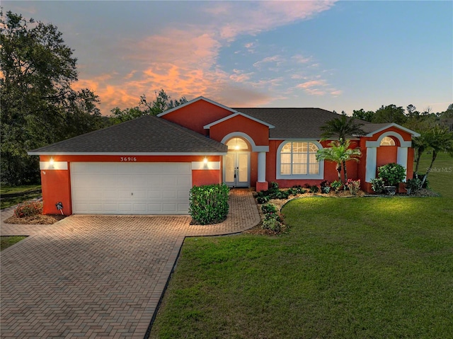 ranch-style house with stucco siding, decorative driveway, a lawn, and a garage