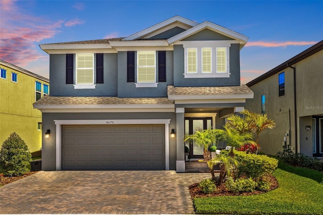 view of front of house featuring a shingled roof, decorative driveway, a garage, and stucco siding