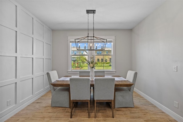 dining space featuring baseboards, an inviting chandelier, wood tiled floor, and a decorative wall