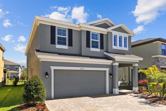 view of front of house with decorative driveway, an attached garage, fence, and stucco siding