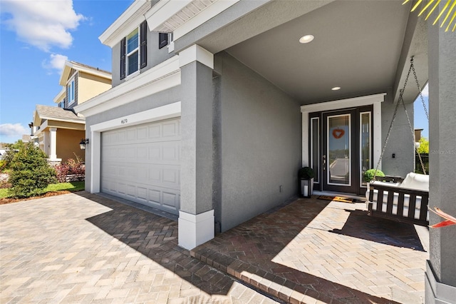 view of exterior entry with decorative driveway, a garage, and stucco siding