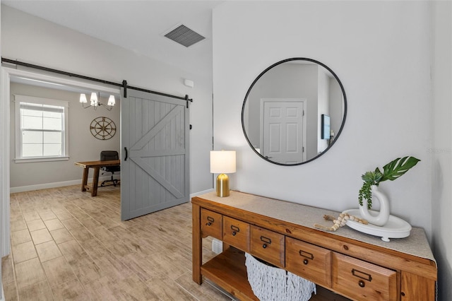 interior space with visible vents, a barn door, baseboards, and light wood finished floors