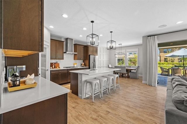 kitchen featuring a kitchen bar, open floor plan, appliances with stainless steel finishes, wall chimney exhaust hood, and light countertops